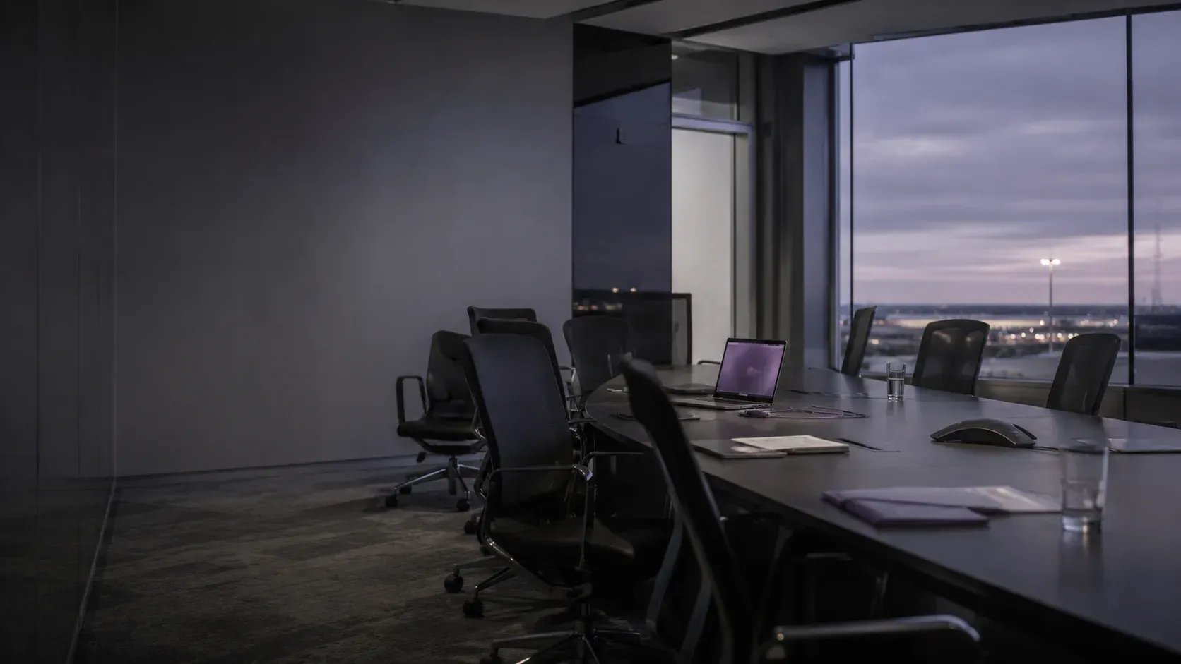 A boardroom at dusk, one screen glowing faint violet
